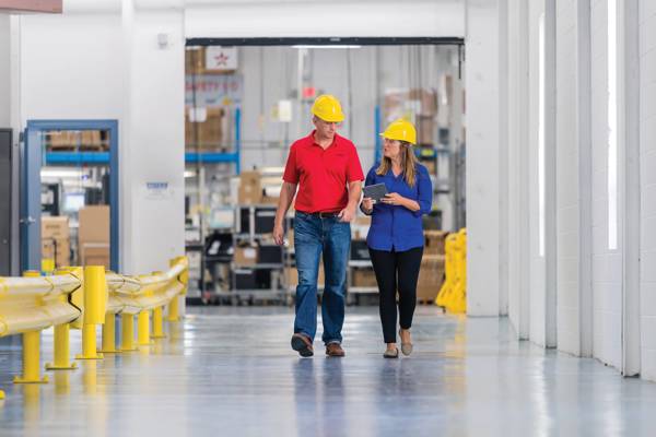 A man and a woman talking and walking through a warehouse holding a tablet