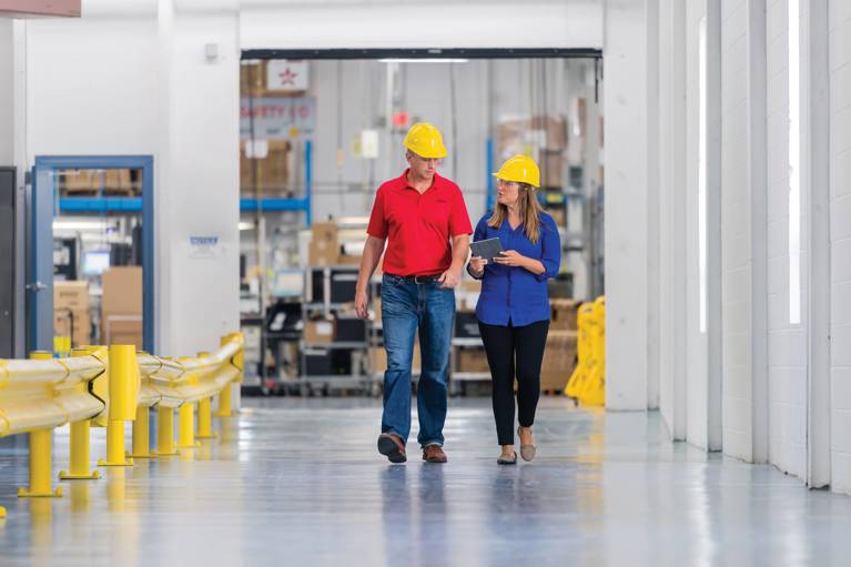 A man and a woman talking and walking through a warehouse holding a tablet