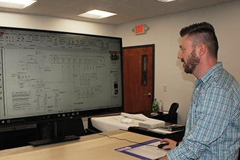 man looking at a large monitor that is displaying electrical drawings