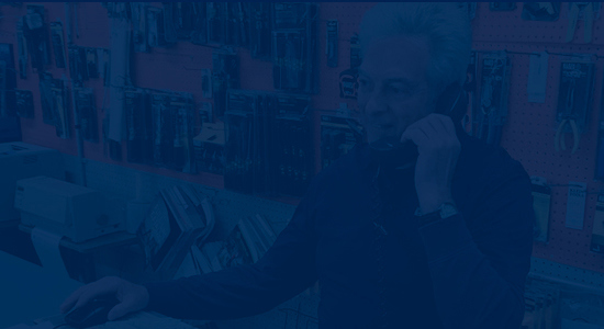 blue overlay image with a man standing behind a retail counter on the phone