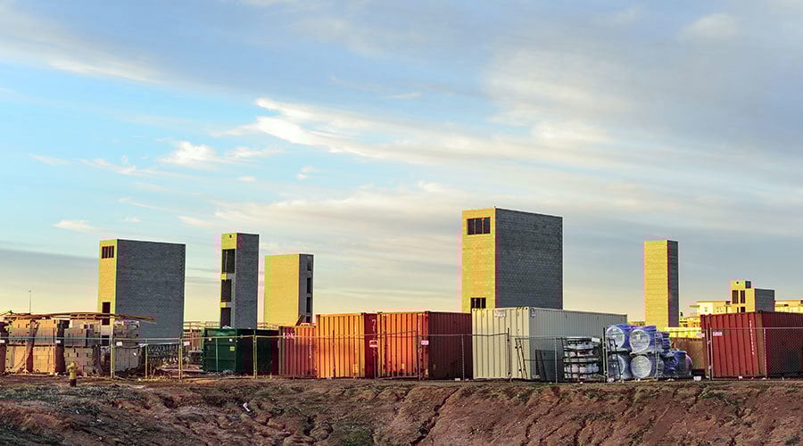Overview of the construction site of a multifamily development, featuring brick towers, various construction materials, and shipping containers